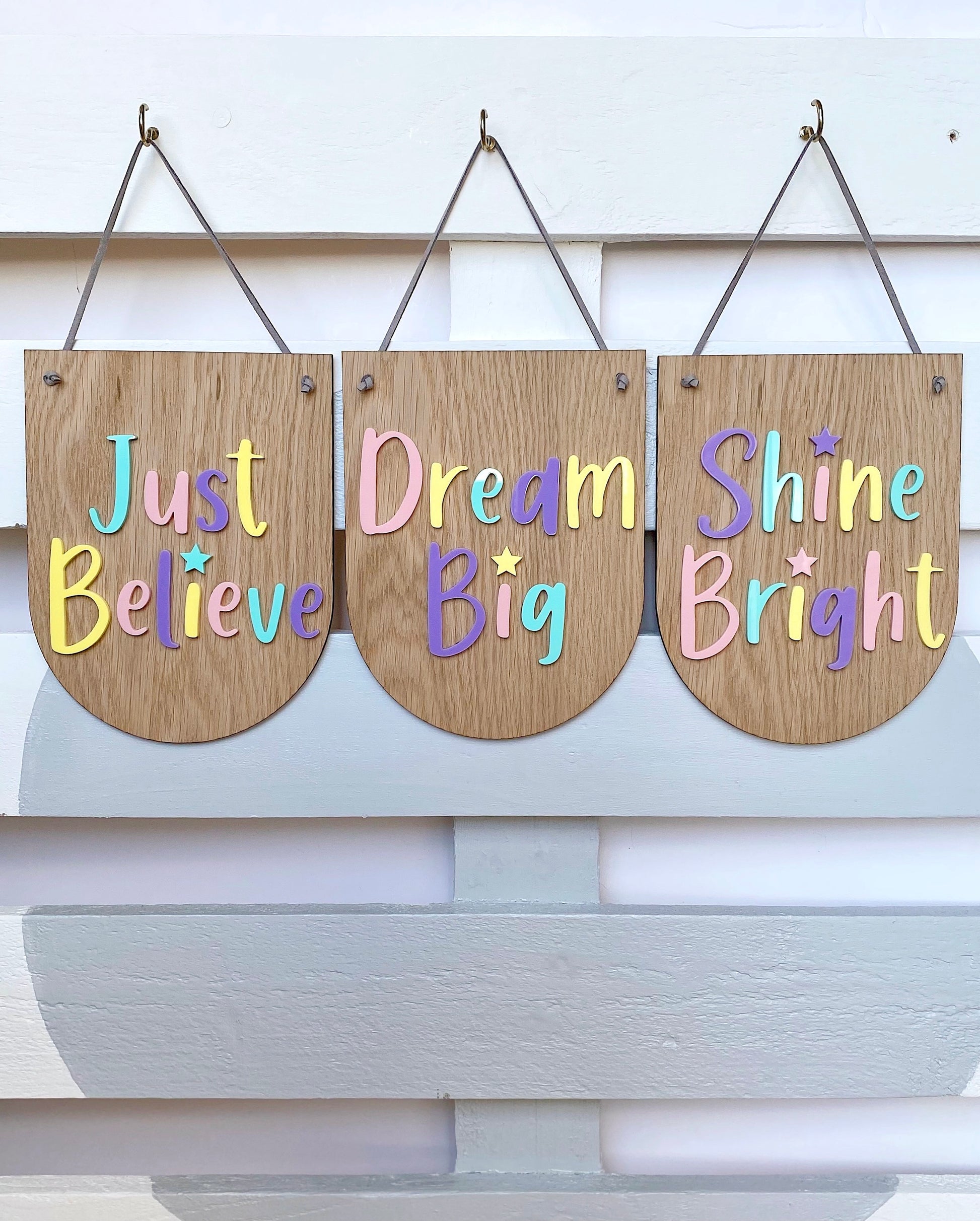 3 wooden plaques in a scalloped design with the words Just Believe, Dream Big and Shine Bright in colourful lettering