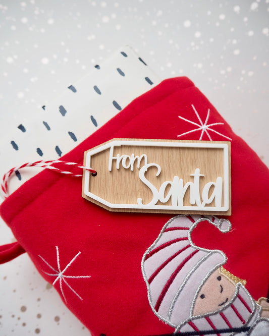 wooden gift tag with the words From Santa in white acrylic. Attached to a Christmas stocking with a present
