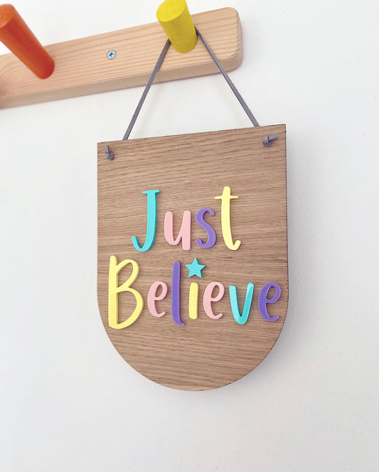 Wooden plaque with the words Just Believe attached in multicoloured pastel acrylic letters
