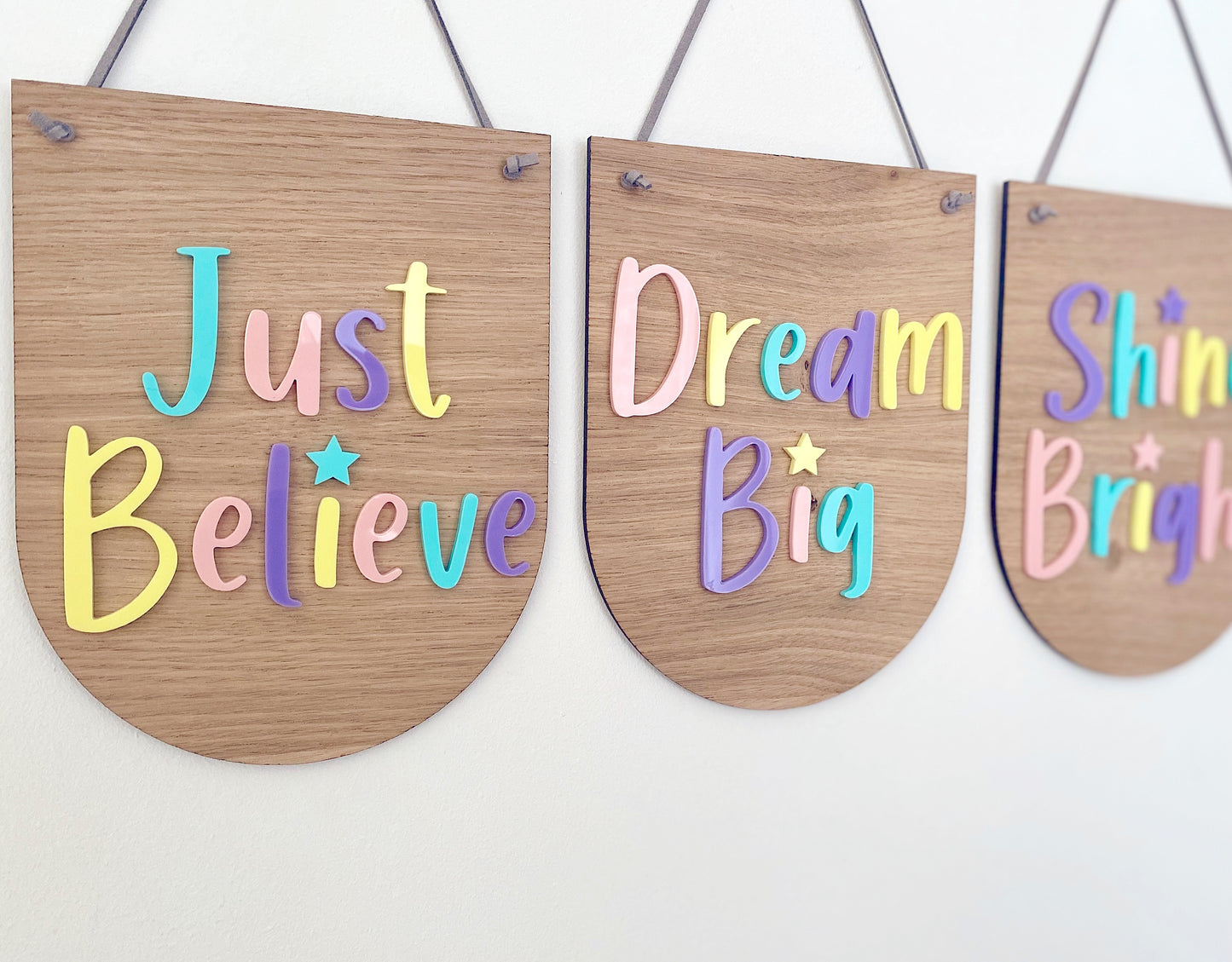 3 coordinating wooden plaques in a scalloped designs. Multicoloured pastel lettering on each saying - Just Believe, Dream Big and Shine Bright