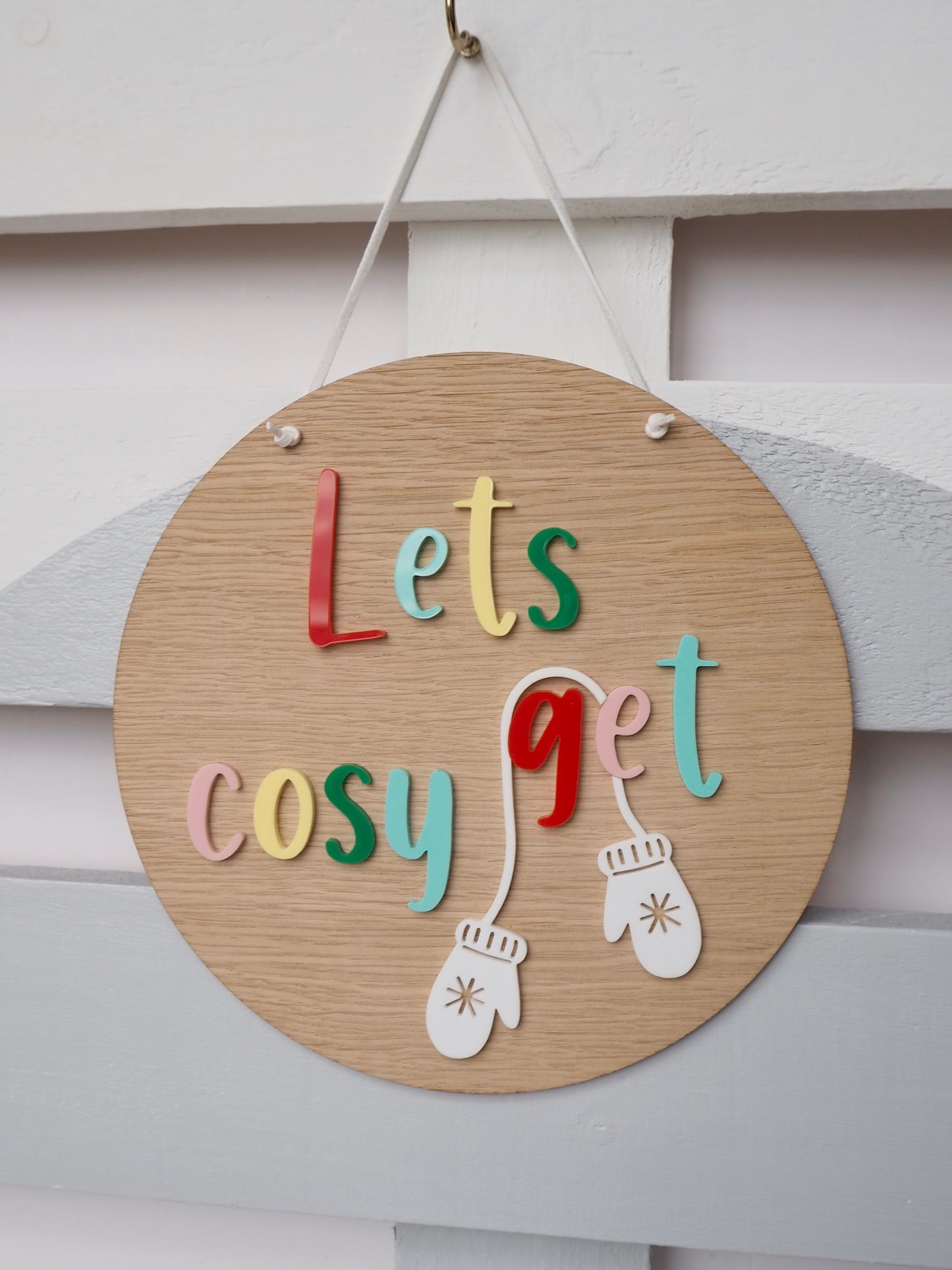 Wooden plaque with multicoloured letting in acrylic saying lets get cosy. 