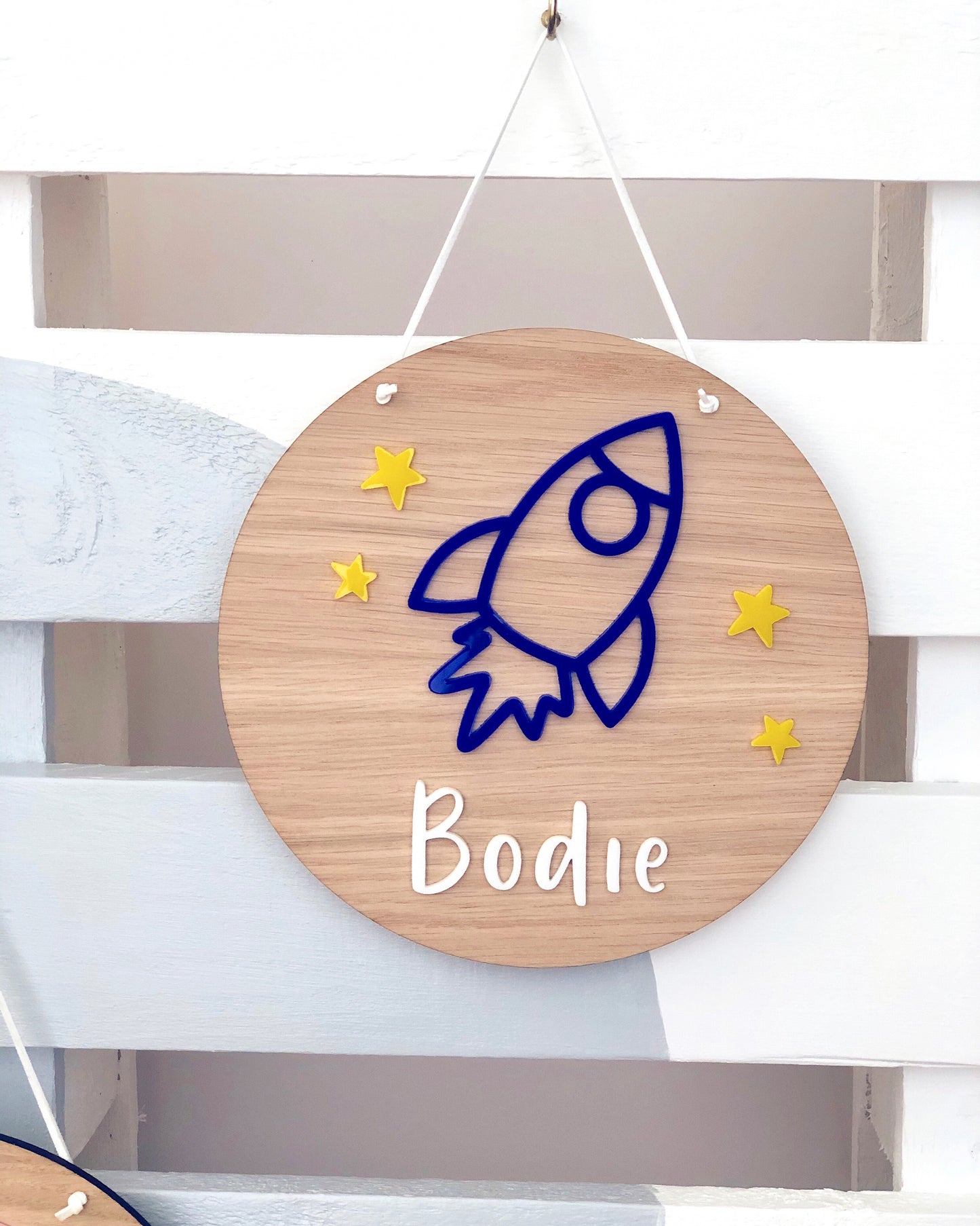 wooden plaque with acrylic blue rocket and yellow stars. Personlised with a name in white acrylic letters