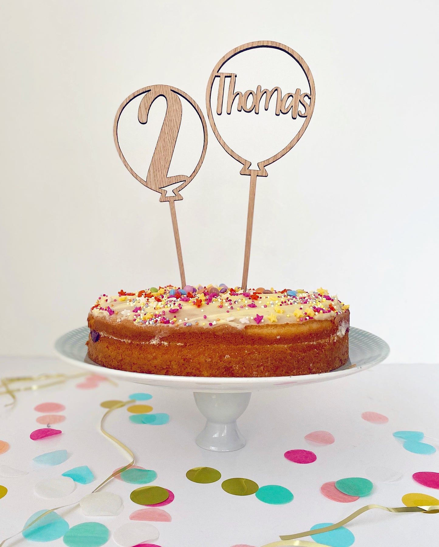 Birthday cake with sprinkles and 2 wooden balloon shaped cake toppers with the age and name laser cut out