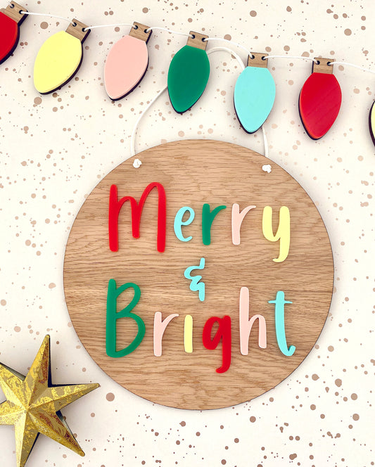 Wooden plaque with the words Merry & Bright in multicoloured acrylic letters