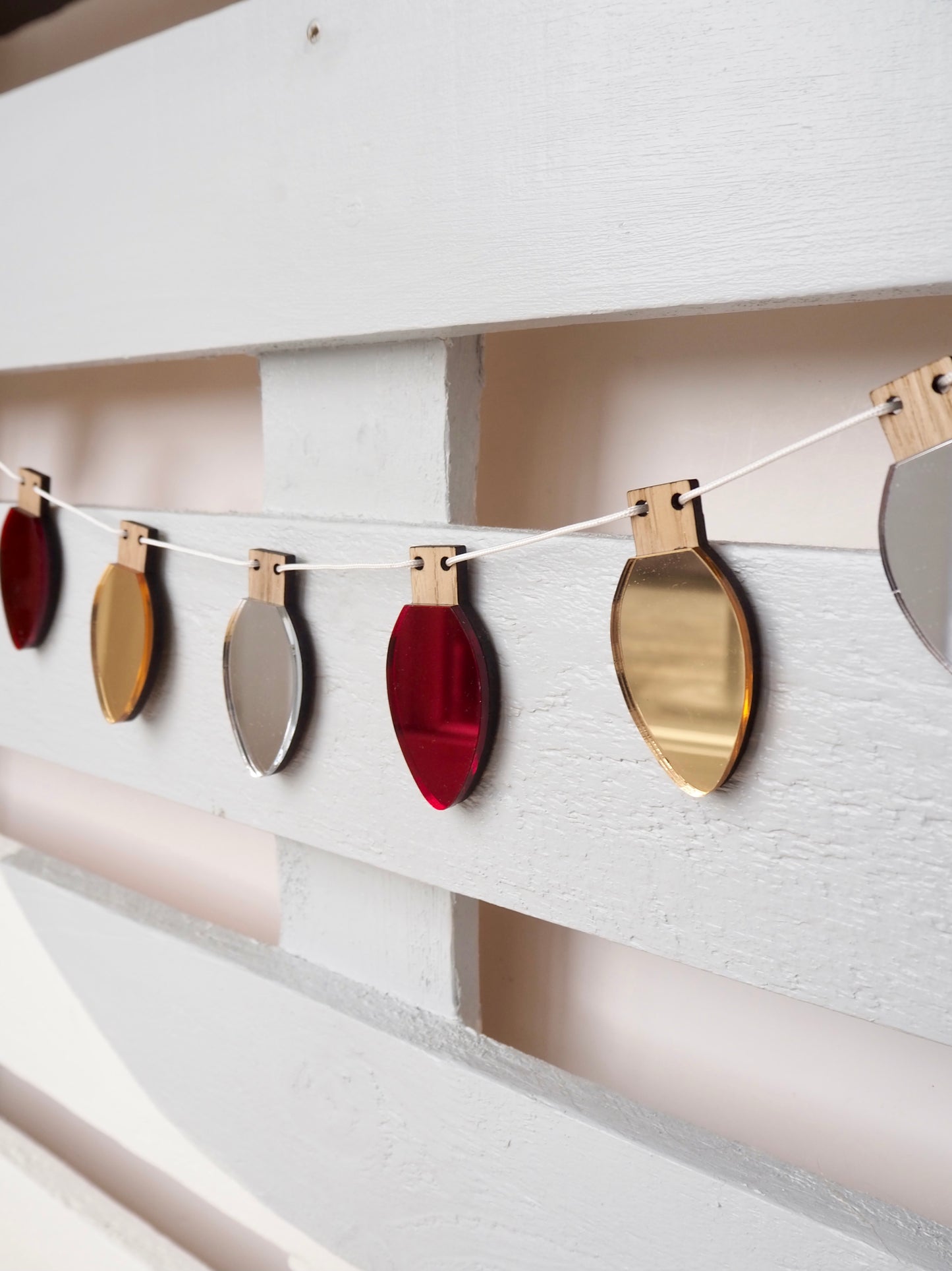 Gold, sliver and red metallic fairy light shapes strung on white cord to create a garland