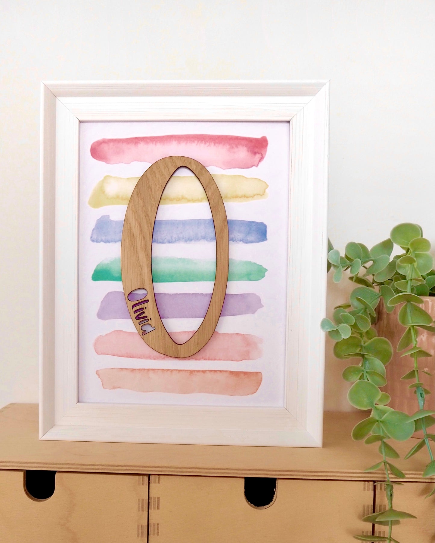 multicoloured striped watercolour print in a white frame with a wooden O and the name Olivia cut from it